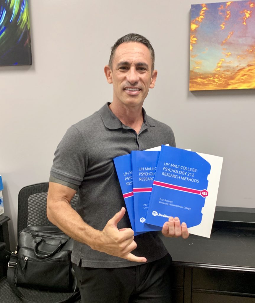 Man holding print open educational resource textbooks and smiling at the camera